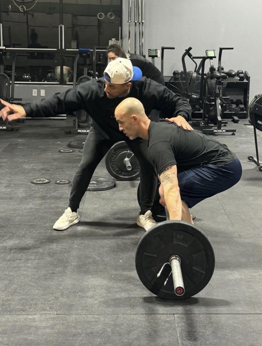 A coach guiding a member through a deadlift